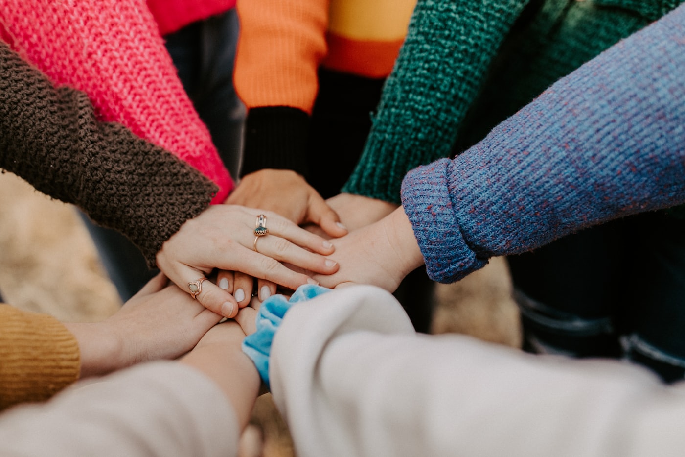 A group stacking their hands together in colourful jumpers, showing support and unity